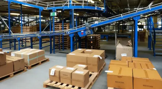Interno di un magazzino automatizzato con sistemi di nastri trasportatori e pacchi pronti per la spedizione in tutta Italia.